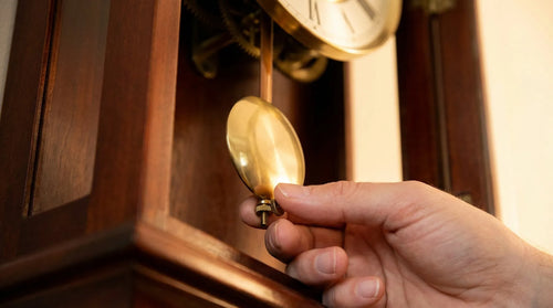 Close-up of fingers adjusting regulation nut beneath brass pendulum bob on grandfather clock