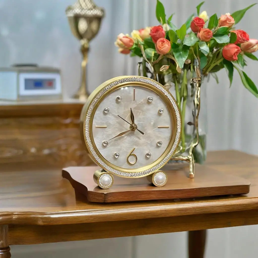 Silent Table Clock - Feynor, a gold-trimmed analog clock with pearl-like accents and crystal markers, elegantly displayed on a wooden base amidst fresh roses, embodies classic style and craftsmanship.