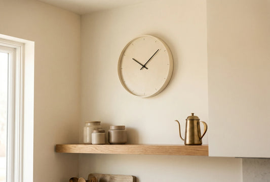 Round wall clock in a calm modern kitchen with oak shelf and warm morning light