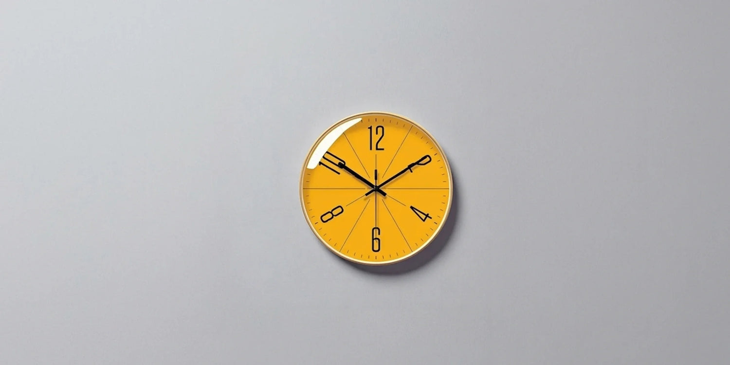 decorative wall clock on a teal wall, time at 10:10, above a wooden sideboard with a glass vase and a hardcover book.