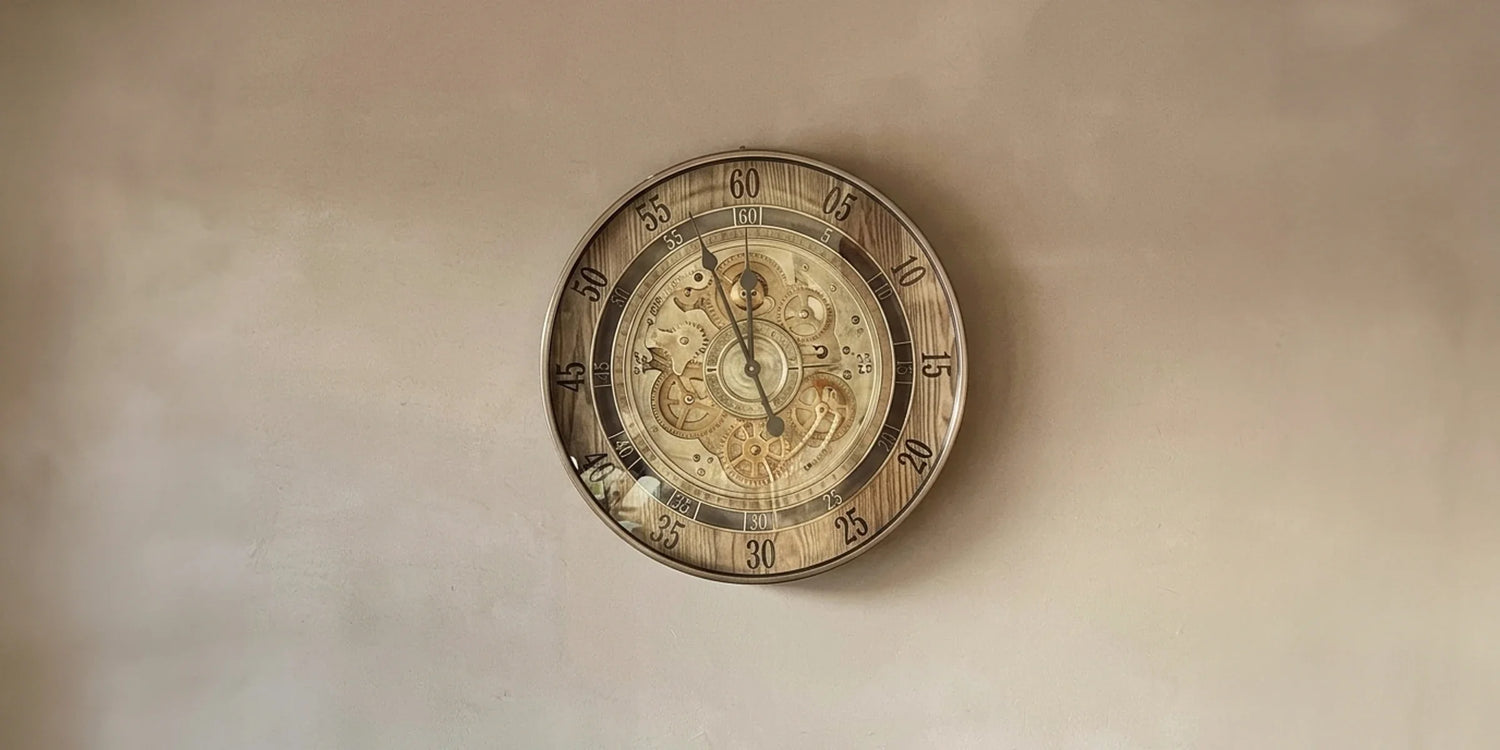 A decorative round clock with a gold frame and Roman numerals hangs above a wooden console table, featuring a beige vase with eucalyptus and a ceramic lamp.