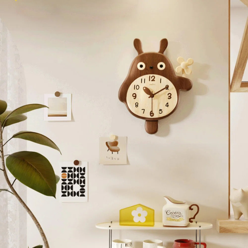 Small decorative wall clocks - Veynor A charming wooden clock, shaped like a chubby animal holding a flower, complements a cozy wall setup with art prints, a shelf, and a white cat figurine.