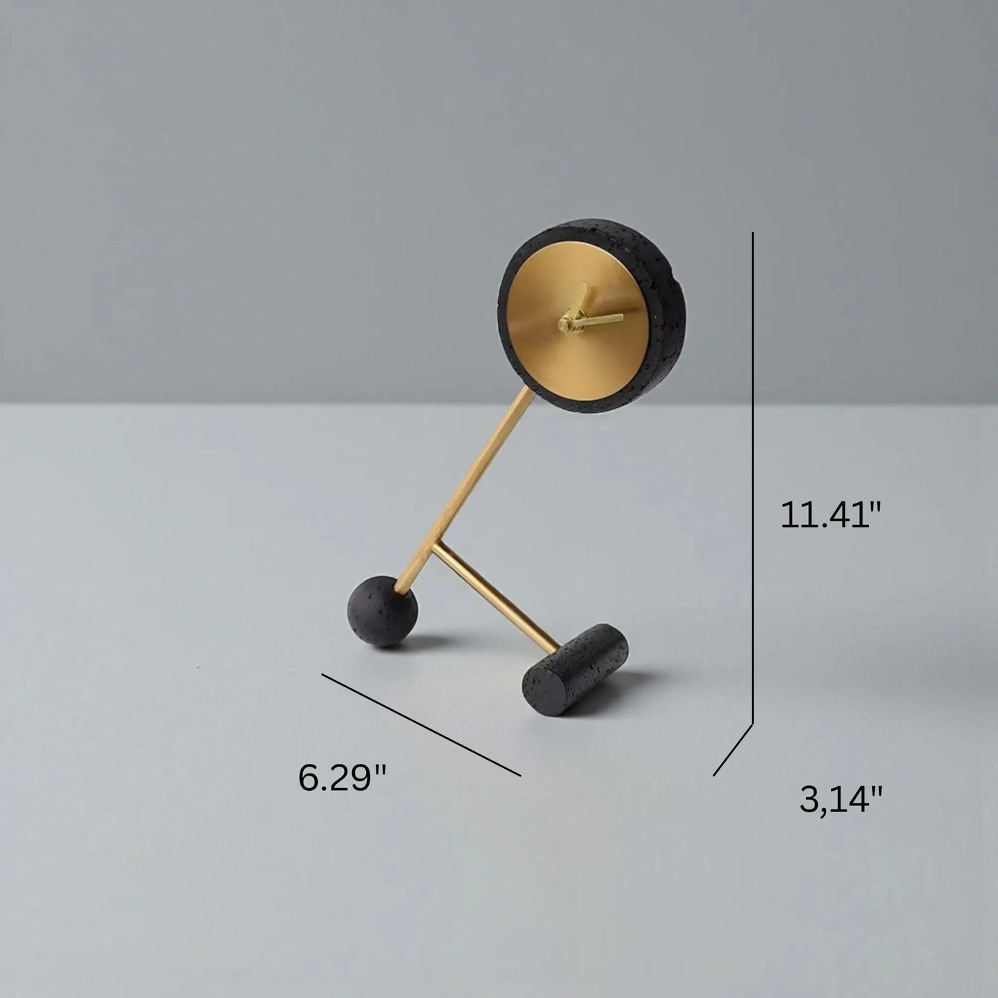 Metal Tabletop Clock - Winsley features a brass-colored open-face design with decorative gears, mounted on a black stone-like asymmetrical stand with spherical and cylindrical feet, adding industrial charm.