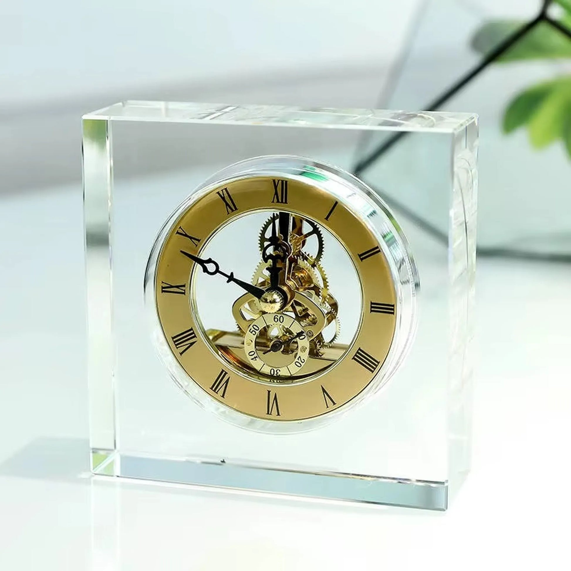 Crystal tabletop clock - Dunley: A clear-glass block elegantly displays its gold-tone skeleton movement, surrounded by a gold dial with black Roman numerals, showcasing intricate gears and a small seconds dial.