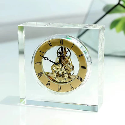 Crystal tabletop clock - Dunley: A clear-glass block elegantly displays its gold-tone skeleton movement, surrounded by a gold dial with black Roman numerals, showcasing intricate gears and a small seconds dial.