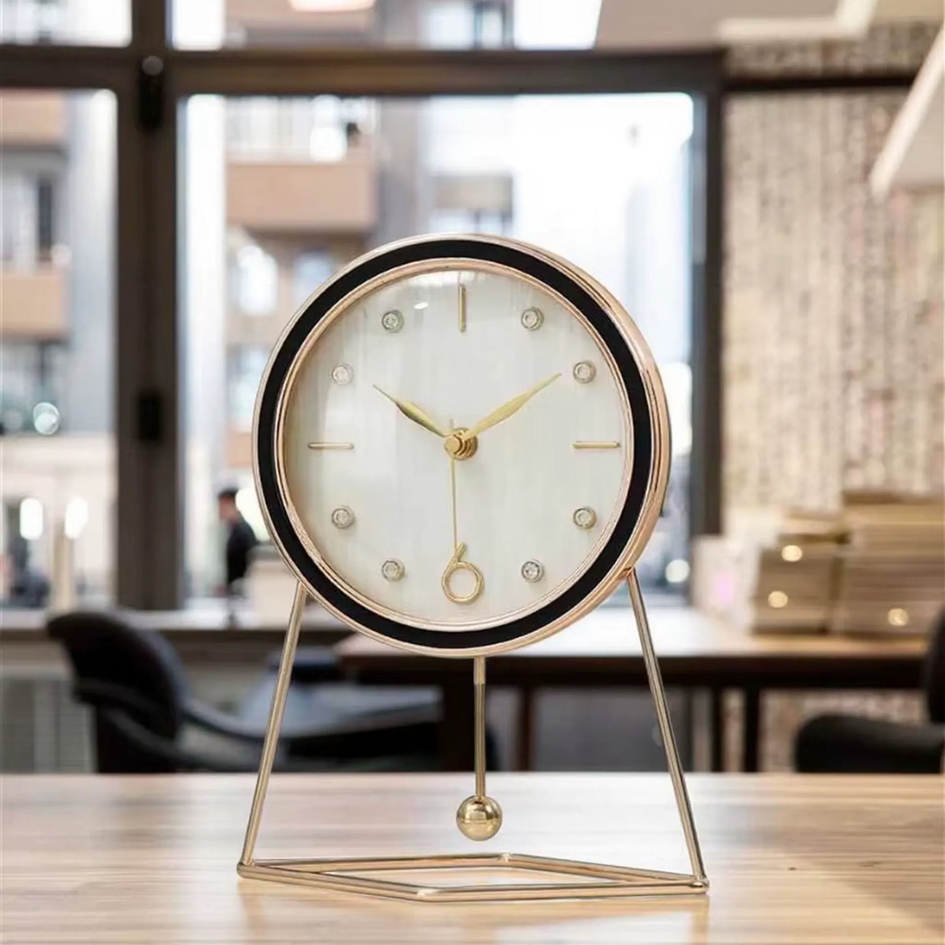 Pendulum Table Clock - Dralen: A small, round desk clock with a white face and gold-tone accents, elegantly mounted on a minimalist triangular stand. Features a swinging pendulum for a dynamic touch.