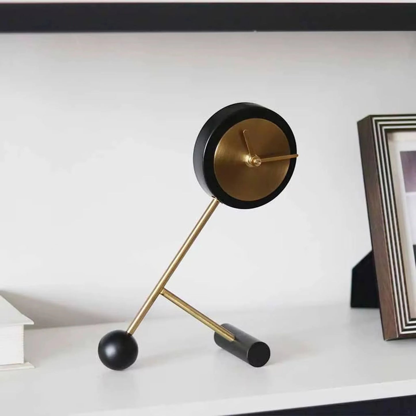 Metal Tabletop Clock - Winsley features a round brass-tone clock-face within a black housing, perched on angled brass rods. Its open-face design reveals decorative gears, adding industrial charm to any setting.