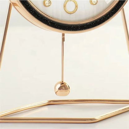 Pendulum Table Clock - Dralen: A gold-tone metal desktop piece with a minimalist circular frame, featuring a black starry rim and a swinging brass pendulum, blending classic style with modern elegance.