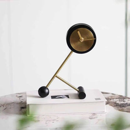 Metal Tabletop Clock - Winsley: A stylish desk clock with a brass-colored dial and decorative gears, perched on angled brass rods, exuding industrial charm atop a closed book.