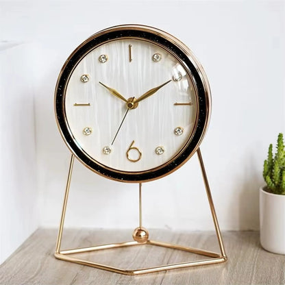 The Dralen Pendulum Table Clock features a white face with gold accents, a minimalist gold-wire stand, and a swinging pendulum, complemented by a potted succulent for a modern, elegant display.