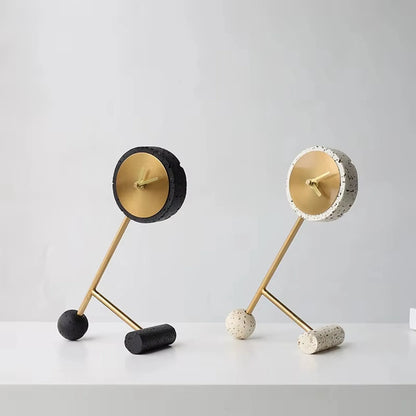 Metal Tabletop Clock - Winsley: Two sculptural, minimalist clocks with gold-toned faces and simple hands, featuring angular brass arms on contrasting bases for a playful, tilted design.