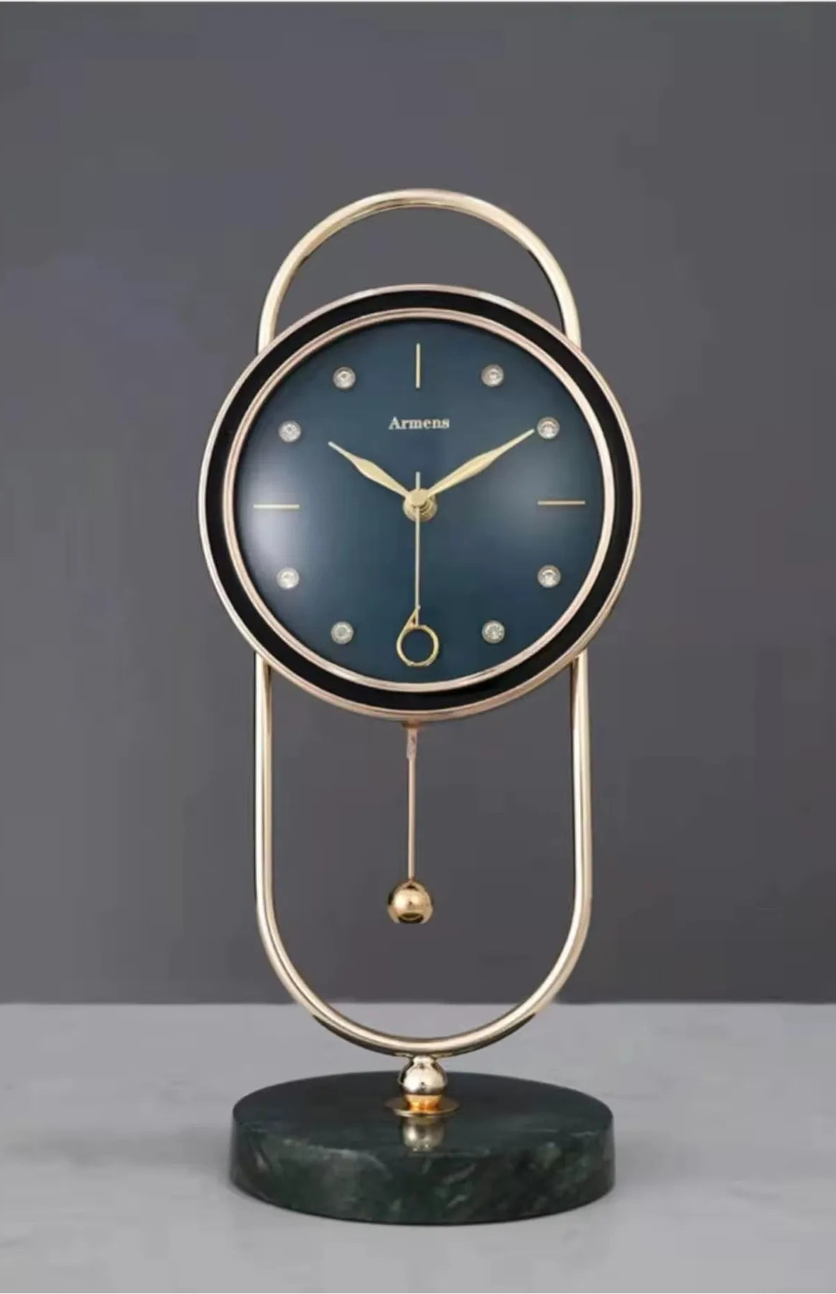 Pendulum Table Clock - Leiton: A modern clock with a deep blue dial, gold hands, crystal markers, and a swinging pendulum, set in a polished gold frame atop a dark green marble base.