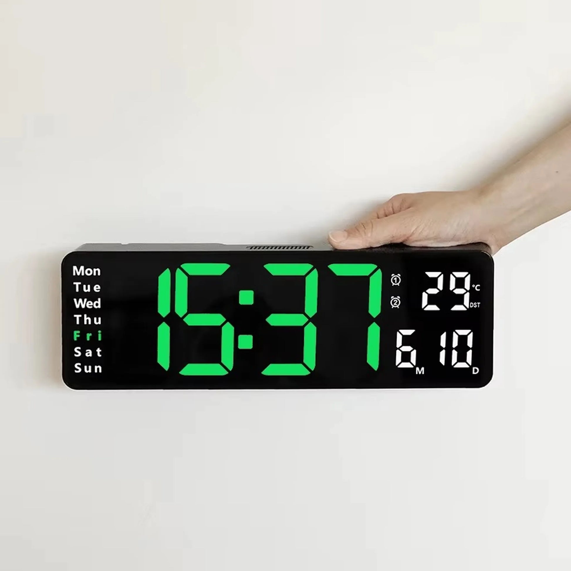 Large digital wall clock - Eldon, displaying time 15:37, day Fri, temperature 29 °C, and date 6 M 10 D, held by a hand, featuring jumbo green LED numerals.