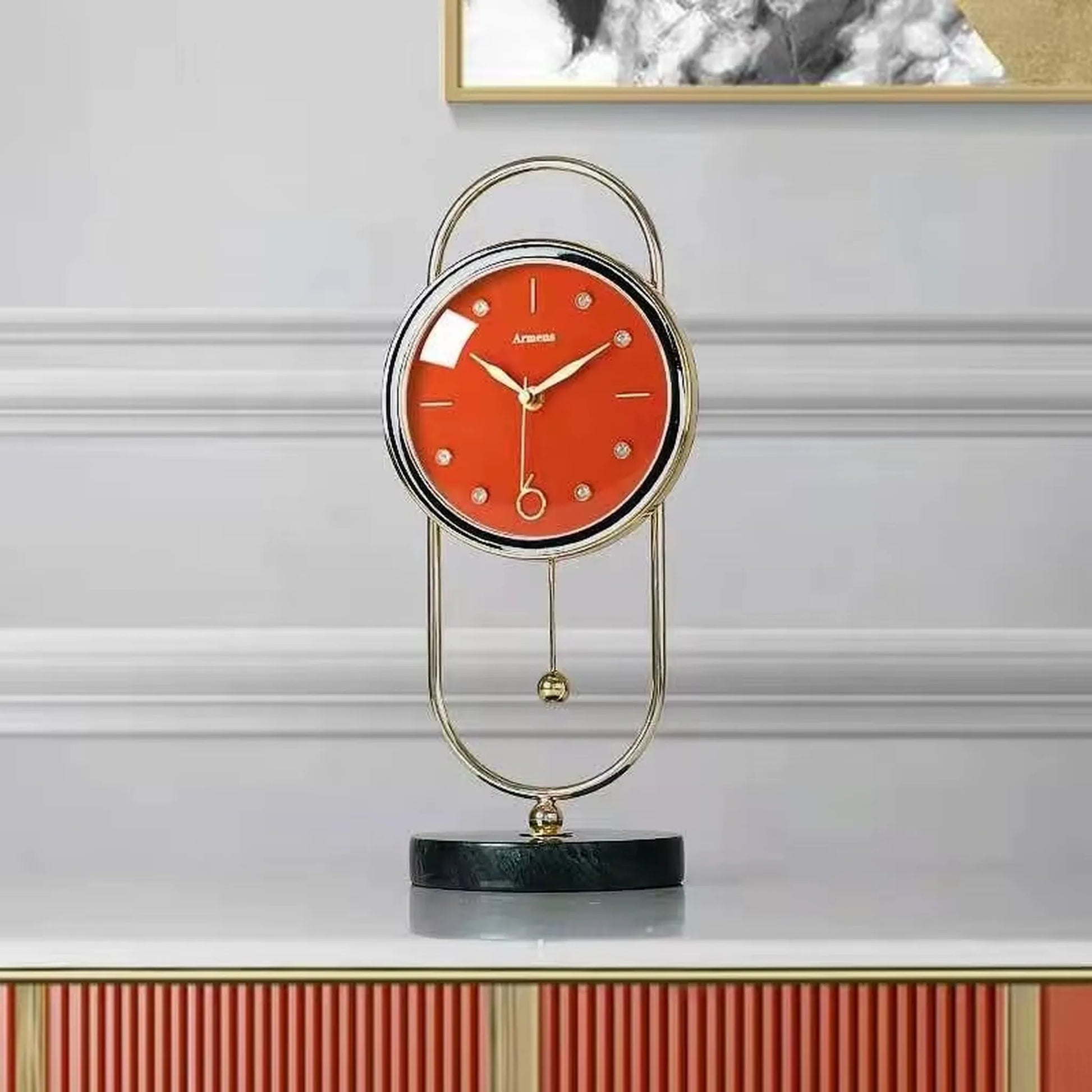 Pendulum Table Clock - Leiton: A modern, elegant table clock with a red dial, gold-tone hands, crystal markers, and a swinging pendulum, all set within an oval gold-metal frame on a marble base.