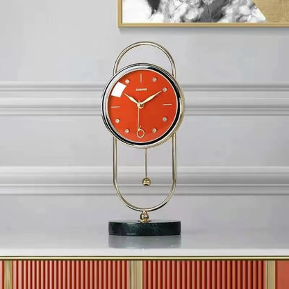 Pendulum Table Clock - Leiton: A modern, elegant table clock with a red dial, gold-tone hands, crystal markers, and a swinging pendulum, all set within an oval gold-metal frame on a marble base.