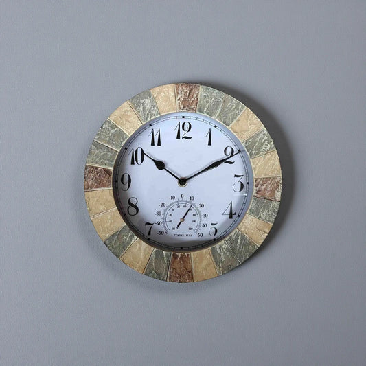 Large outdoor wall clock - Sylva with a multi-colored stone border, black hands, and Arabic numerals on a white dial, featuring a temperature gauge at 6 o'clock, set against a gray wall.