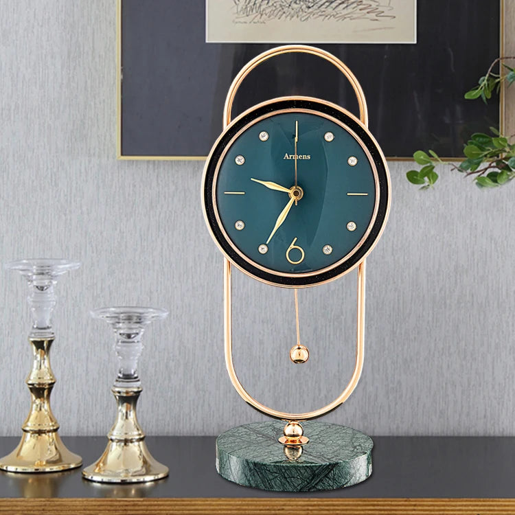 Pendulum Table Clock - Leiton, featuring a teal face with gold accents, suspended in a gold-tone frame with a swinging pendulum, set on a green-veined base, flanked by elegant candlesticks.