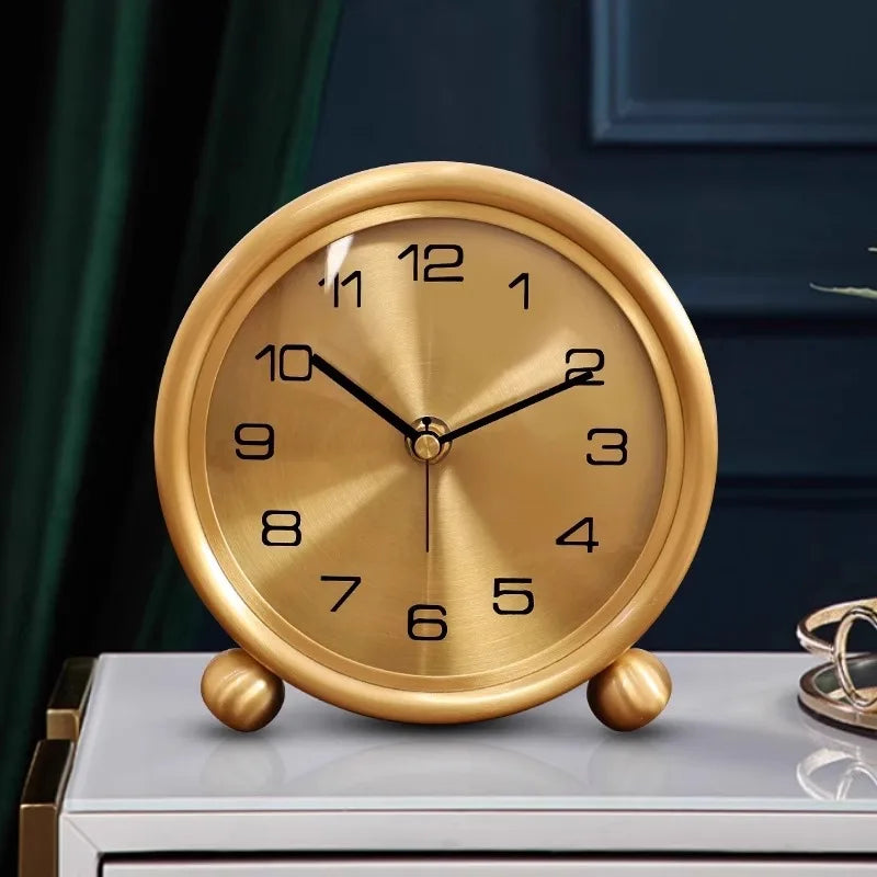 Brass Table Clock - Helric: A round, gold-colored analog clock with black numerals and hands, sitting elegantly on two small ball feet, showcasing traditional elegance for your desk or mantel.