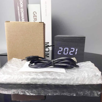 Cube Alarm Clock - Corven, showcasing a wood-grain finish with an LED displaying 20:21, accompanied by a USB cable, instruction sheet, bubble-wrap, and packaging, ideal for modern bedside tables.