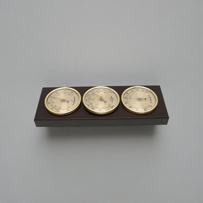Weather Station Wall Clock - Harlton: A wall-mounted instrument featuring brass-rimmed hygrometer, barometer, and thermometer on a dark wooden plaque, embodying classic elegance from The Horologista's collection.