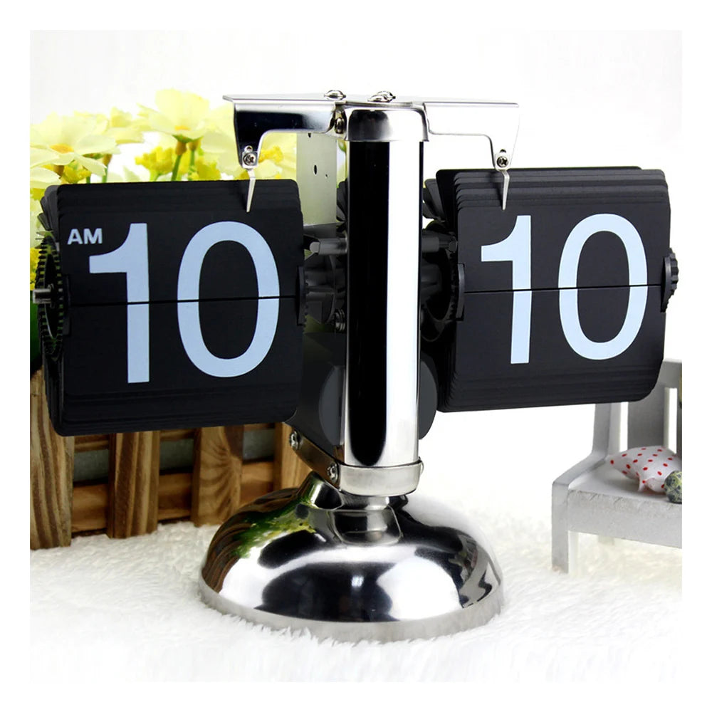 Retro flip clock - Jorrel on a polished stand, displaying “10:10 AM,” with split-flap number cards. A wooden planter with yellow flowers and a decorative chair enhance its timeless design.
