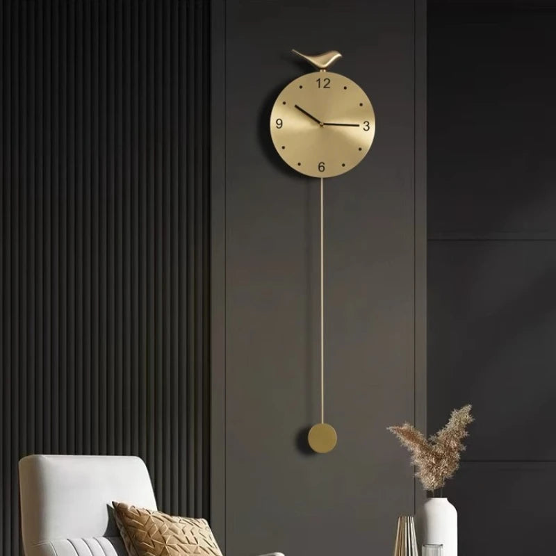 Modern pendulum wall clock - Majesty, features a sleek gold finish with a perched bird and long pendulum, set against a minimalist dark-charcoal paneled wall, creating a sophisticated focal point.
