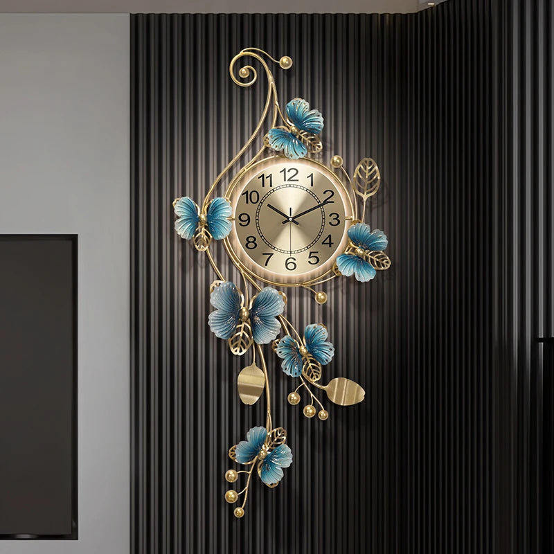 Hanging Wall Clock - Elmsford: A gold-toned round clock with black numerals, surrounded by sculptural metal vines and blue accents, creating an artistic and contemporary wall decor statement.