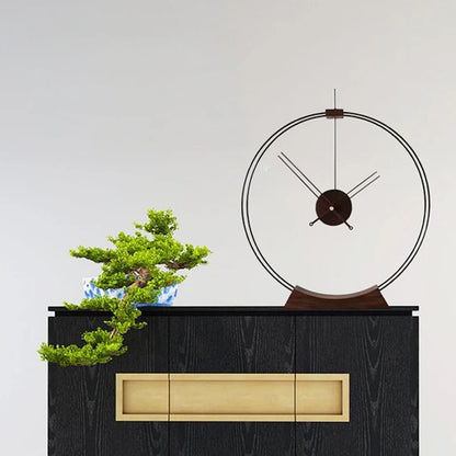 Design table clock - Bexley: A minimalist ring-shaped table clock with exposed hands and central movement atop a wooden base, next to a bonsai on a black-stained cabinet, embodying sleek contemporary style.