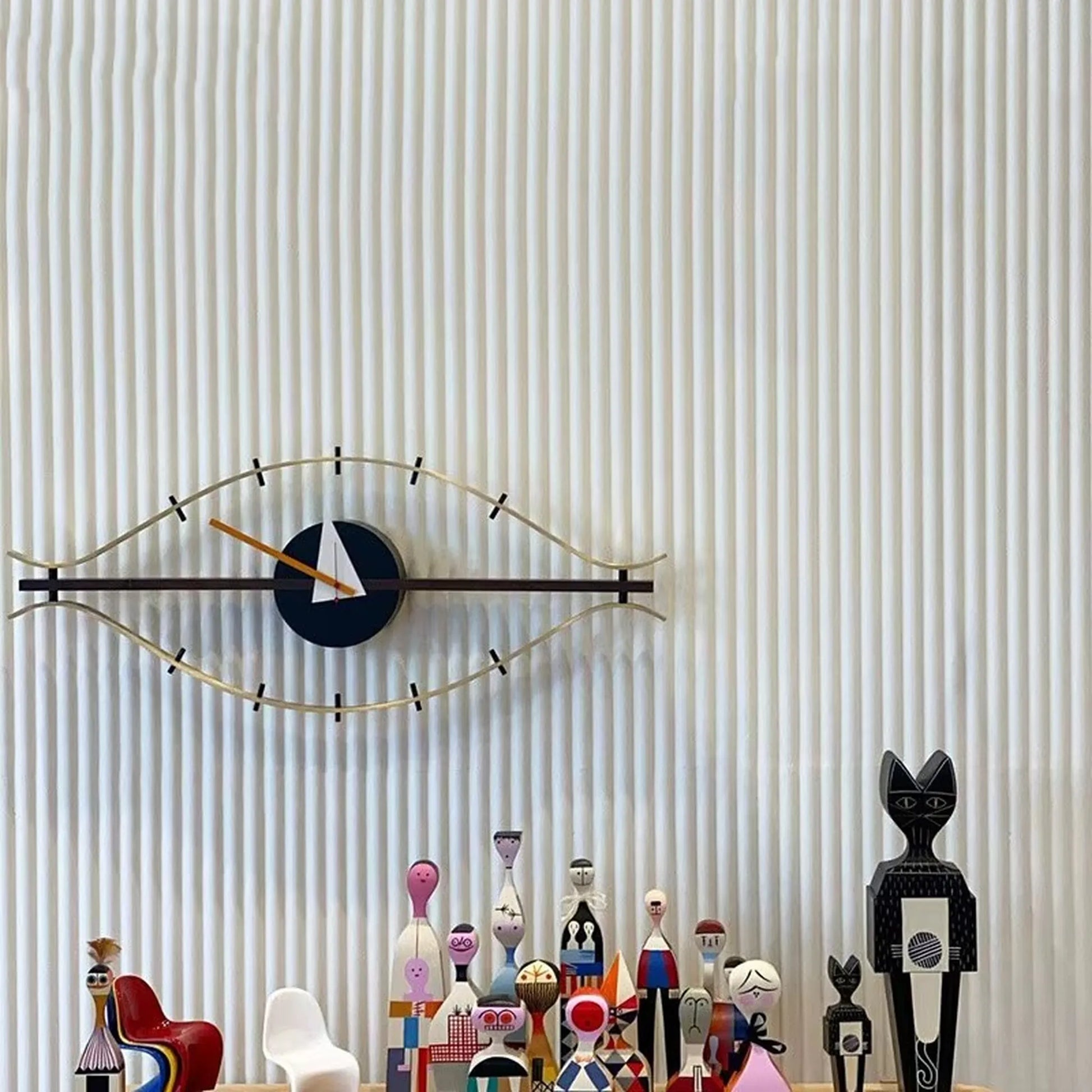 30-inch decorative wall clock - Ashen: A mid-century-modern eye clock with a single hand on a brass outline, complemented by wooden peg-doll figures, creating a striking centerpiece on a ridged wall panel.