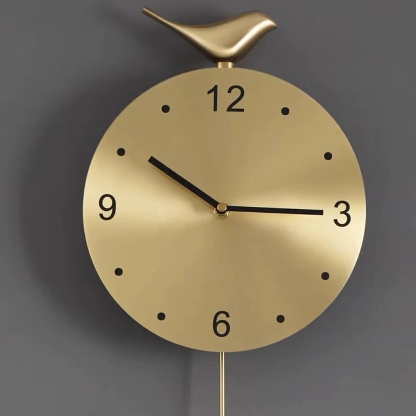 Modern pendulum wall clock - Majesty features a brushed-gold face with minimalist black numerals and dots, a slim pendulum, and a bird figurine, offering an elegant touch to contemporary decor.