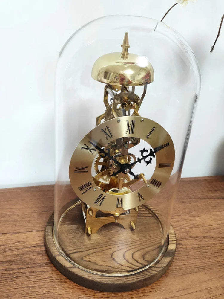 Glass dome clock - Stanley: A brass skeleton mantel clock under a glass dome, featuring exposed gears, Roman numerals, ornate hands, and a passing bell strike movement on a wooden base.