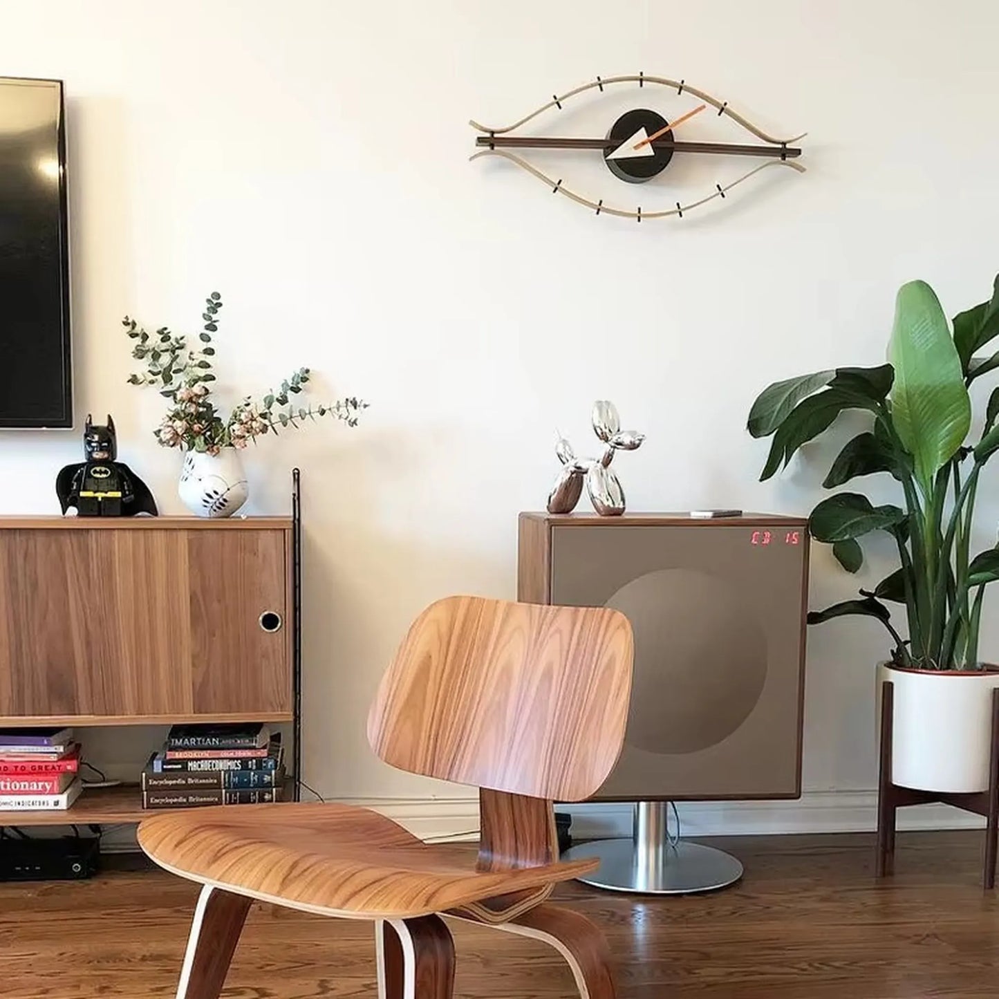 30-inch decorative wall clock - Ashen, a striking eye-shaped design, hangs prominently, adding vintage flair to a mid-century living space with a molded plywood chair and walnut media console.