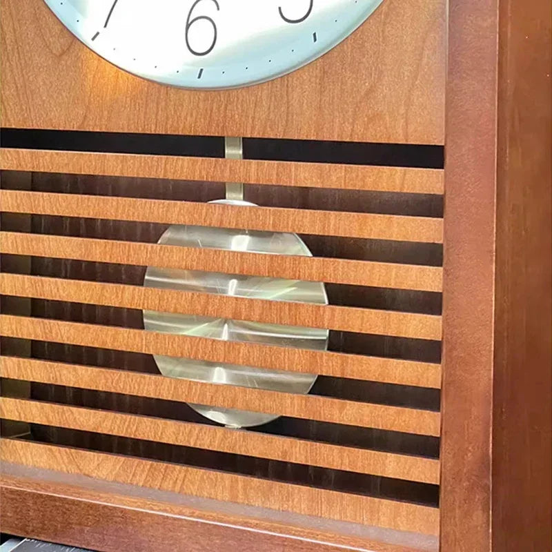Japanese wall Clock - Lexton, featuring a wooden case with a slatted grill showcasing a swinging metal pendulum bob, and a glimpse of the clock face with numbers 7, 6, and 5.