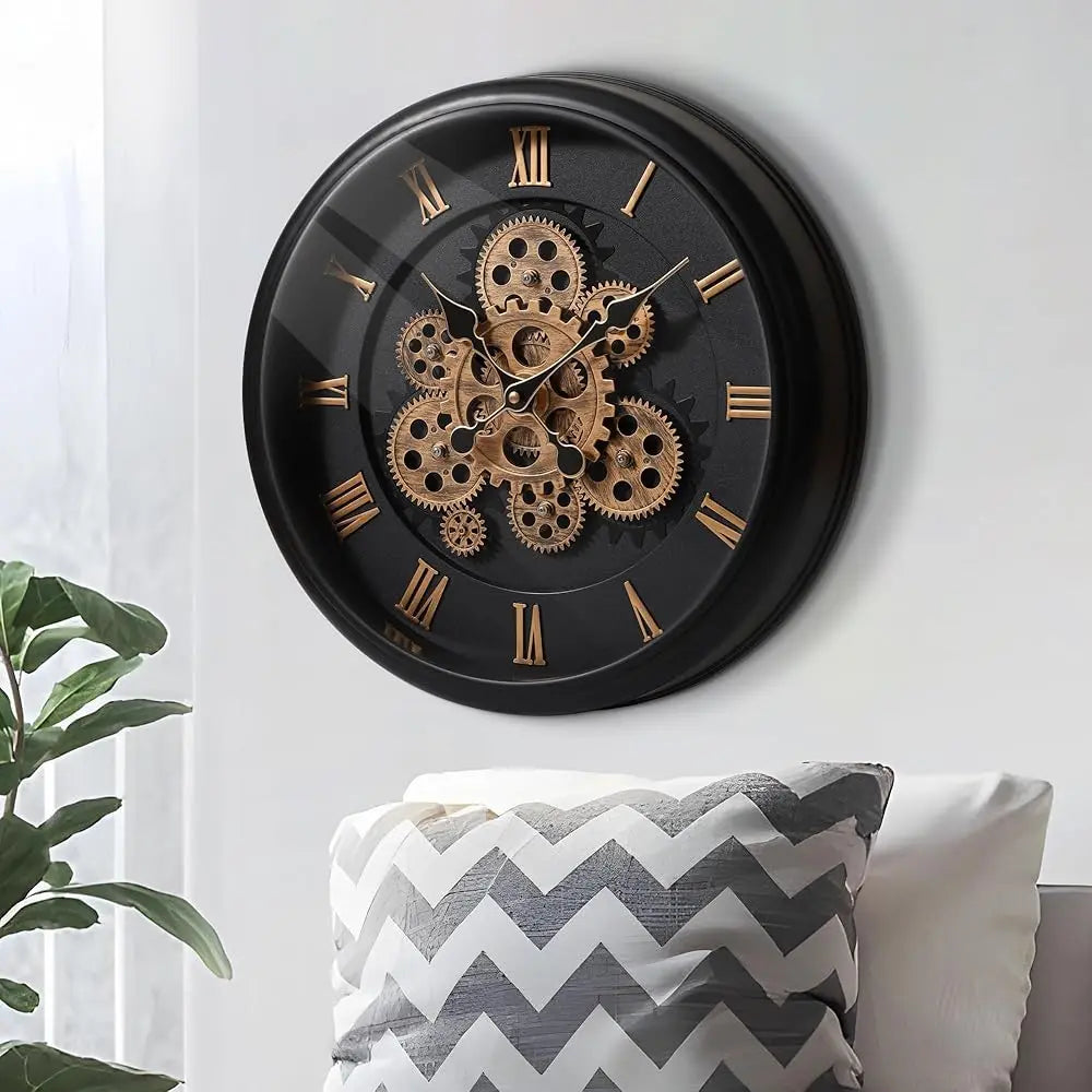 Oversized Wall Clock - Kairos, featuring a black frame with distressed finish, showcases exposed brass gears and Roman numerals. It’s mounted on a light wall, complemented by a nearby leafy houseplant.