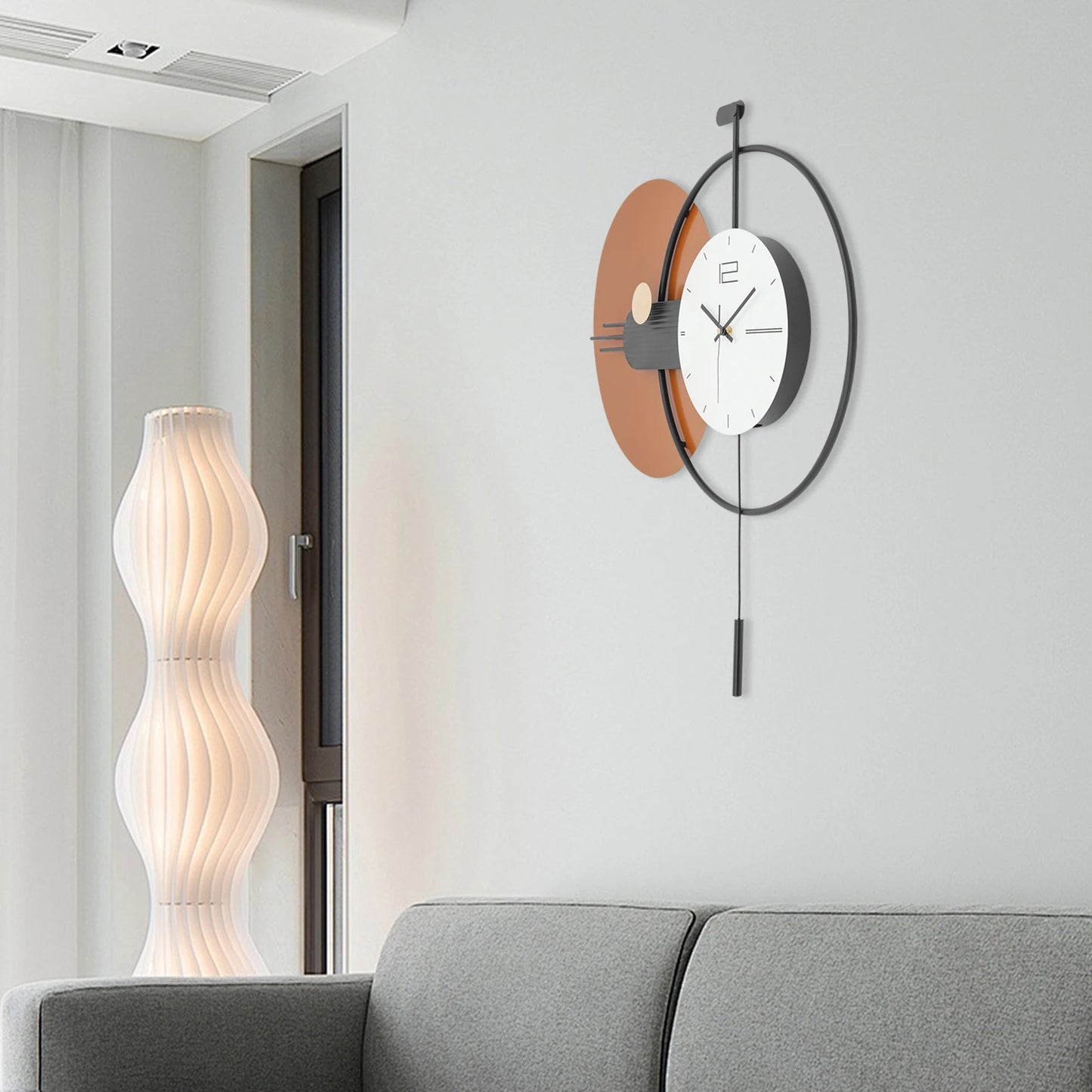 Big Wall Clock Modern - Darrington featured in a minimalist living-room corner, showcasing its sleek design with overlapping circular frames and a slim pendulum, complemented by a light-grey upholstered sofa.