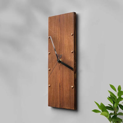 Wood Wall Clock - Stalford: A minimalist clock from The Horologista made from a single vertical linden wood plank, featuring six metal rivets and three black hands, mounted on a wall with a plant nearby.