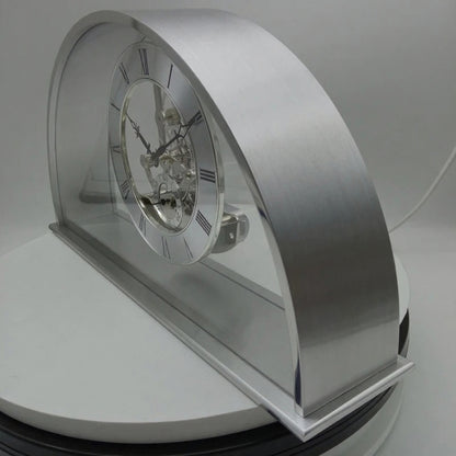 Crystal table clock - Cranley: A modern skeleton desk clock with a transparent face and Roman numerals, showcasing intricate chrome gears within a curved arch frame, set on a sleek rectangular base.