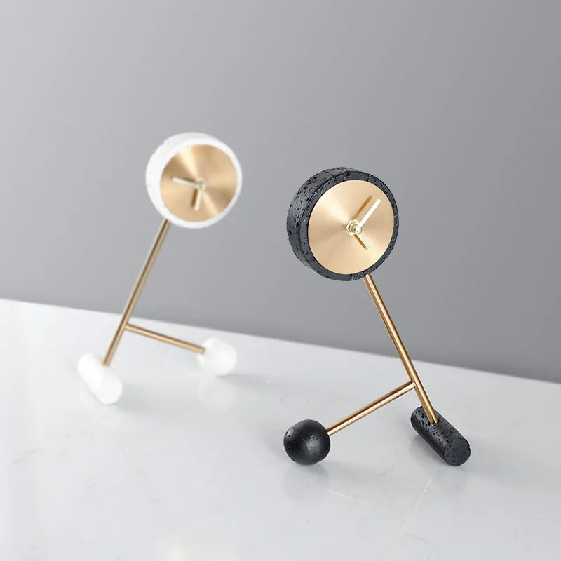 Metal Tabletop Clock - Winsley features a brass-coloured open-face design with stick hands, decorative gears, and textured rings in white and black, mounted on L-shaped rods for an industrial look.