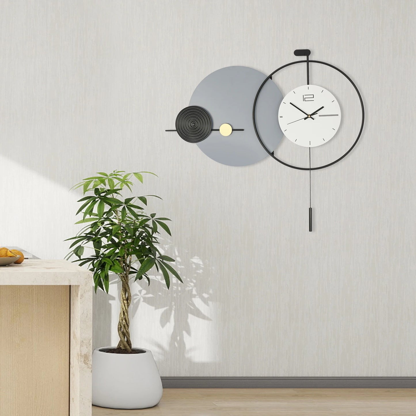 Big Wall Clock Modern - Darrington: A minimalist clock with a matte-gray disc, black metal ring, and brass accent, elegantly framed by a braided-trunk houseplant and light-wood countertop.
