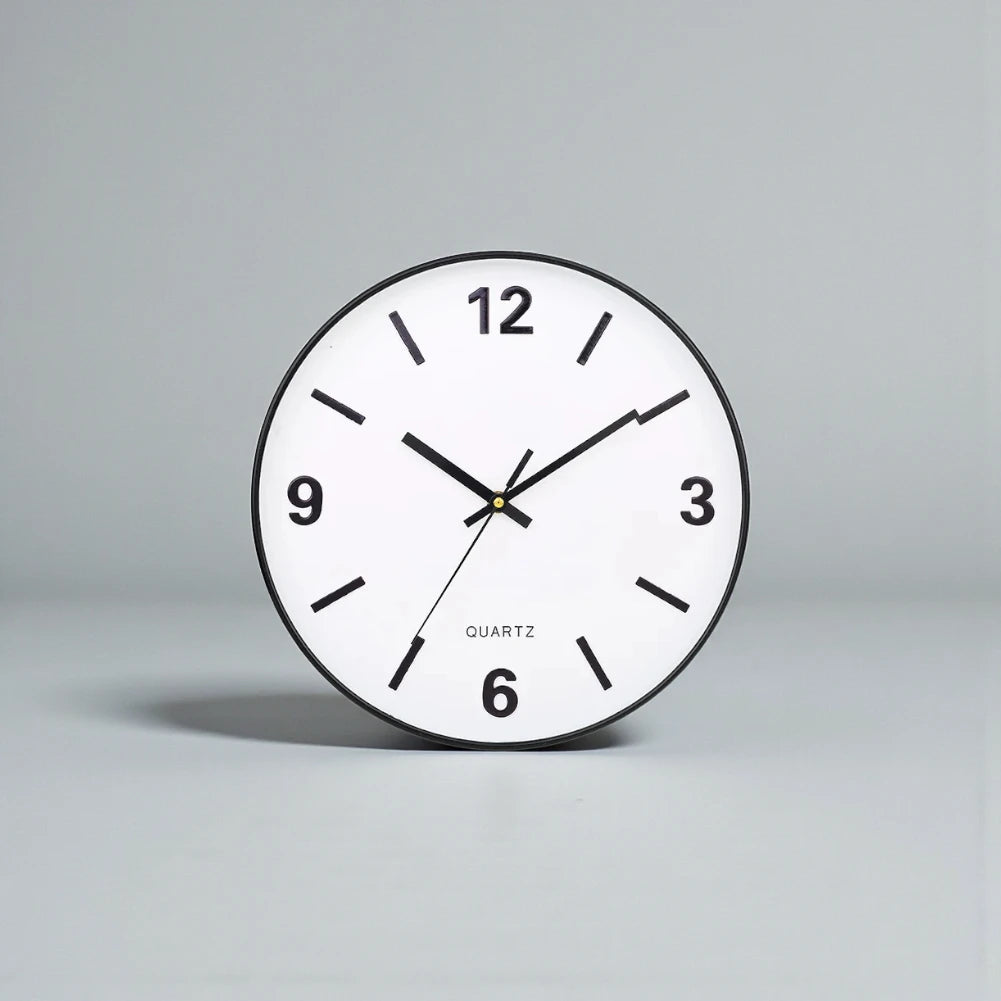 Modern Silent Wall Clock - Densford against a gray backdrop, showcasing its minimalist design with a white face, black hands, bold numerals at quarter hours, and silent quartz movement.