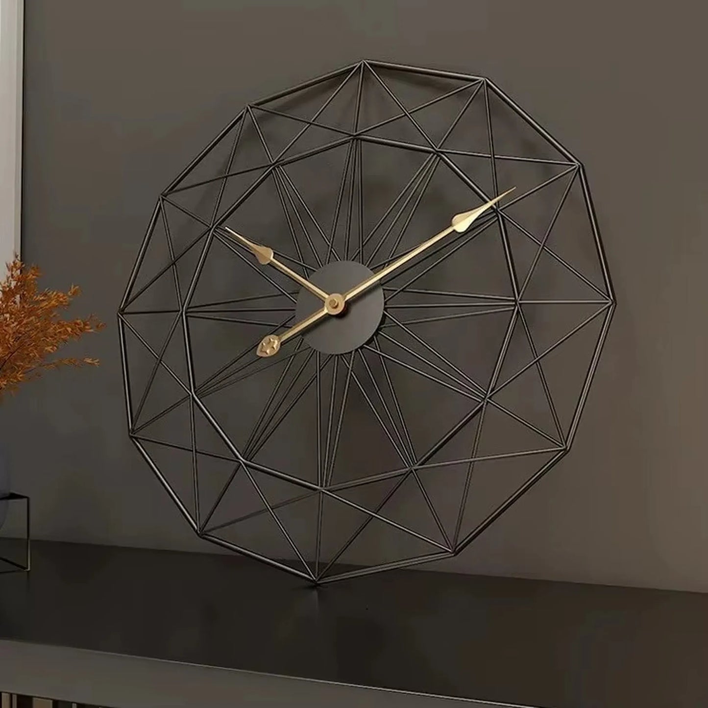 Modern Style Wall Clock - Blenford: A geometric desk clock with a spherical wireframe made from black metal rods, featuring slender gold hands, displayed on a dark tabletop beside a glass container with dried foliage.