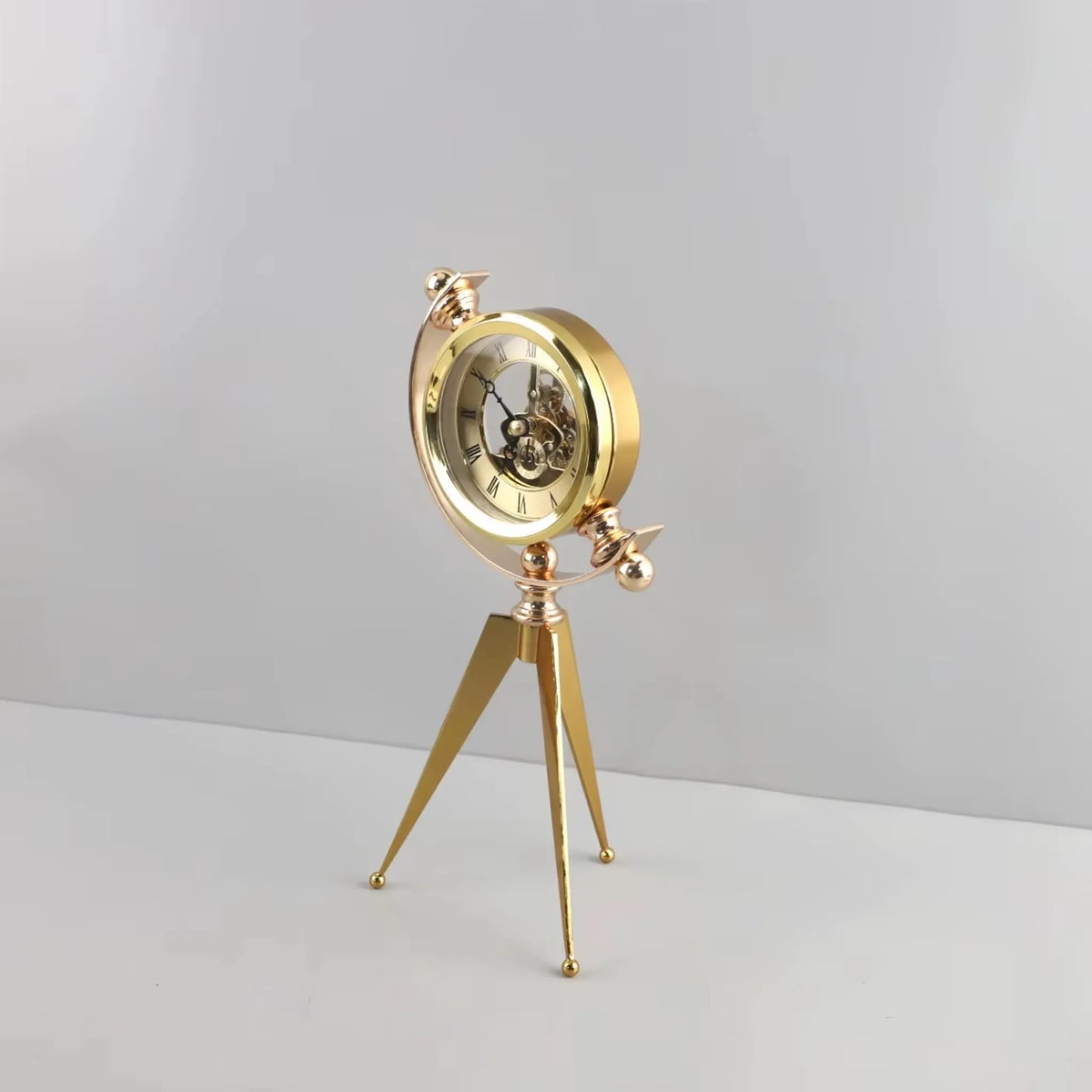 Vintage Table Clock - Gorven: A gold-tone mechanical skeleton clock with visible gears, mounted in a circular frame on a tripod stand, showcasing Roman numerals, perfect for adding vintage charm to any tabletop.