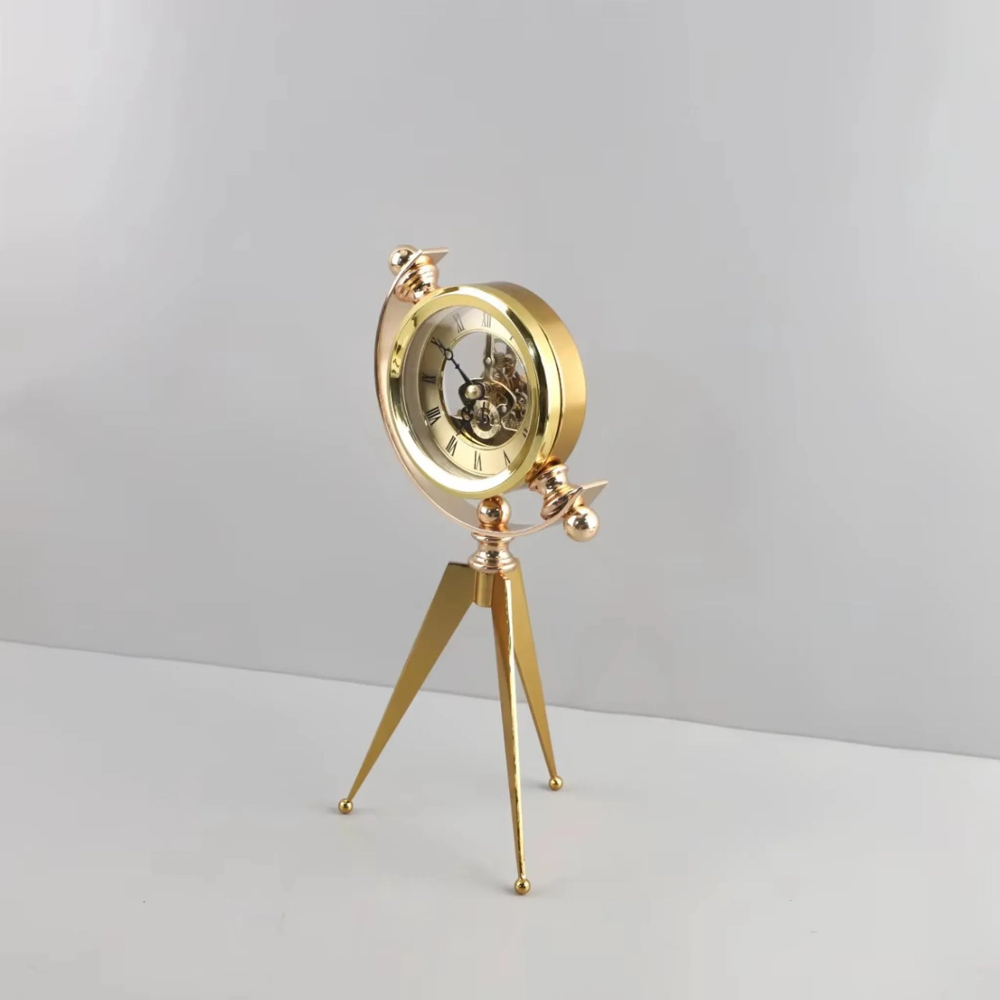Vintage Table Clock - Gorven: A gold-tone mechanical skeleton clock with visible gears, mounted in a circular frame on a tripod stand, showcasing Roman numerals, perfect for adding vintage charm to any tabletop.