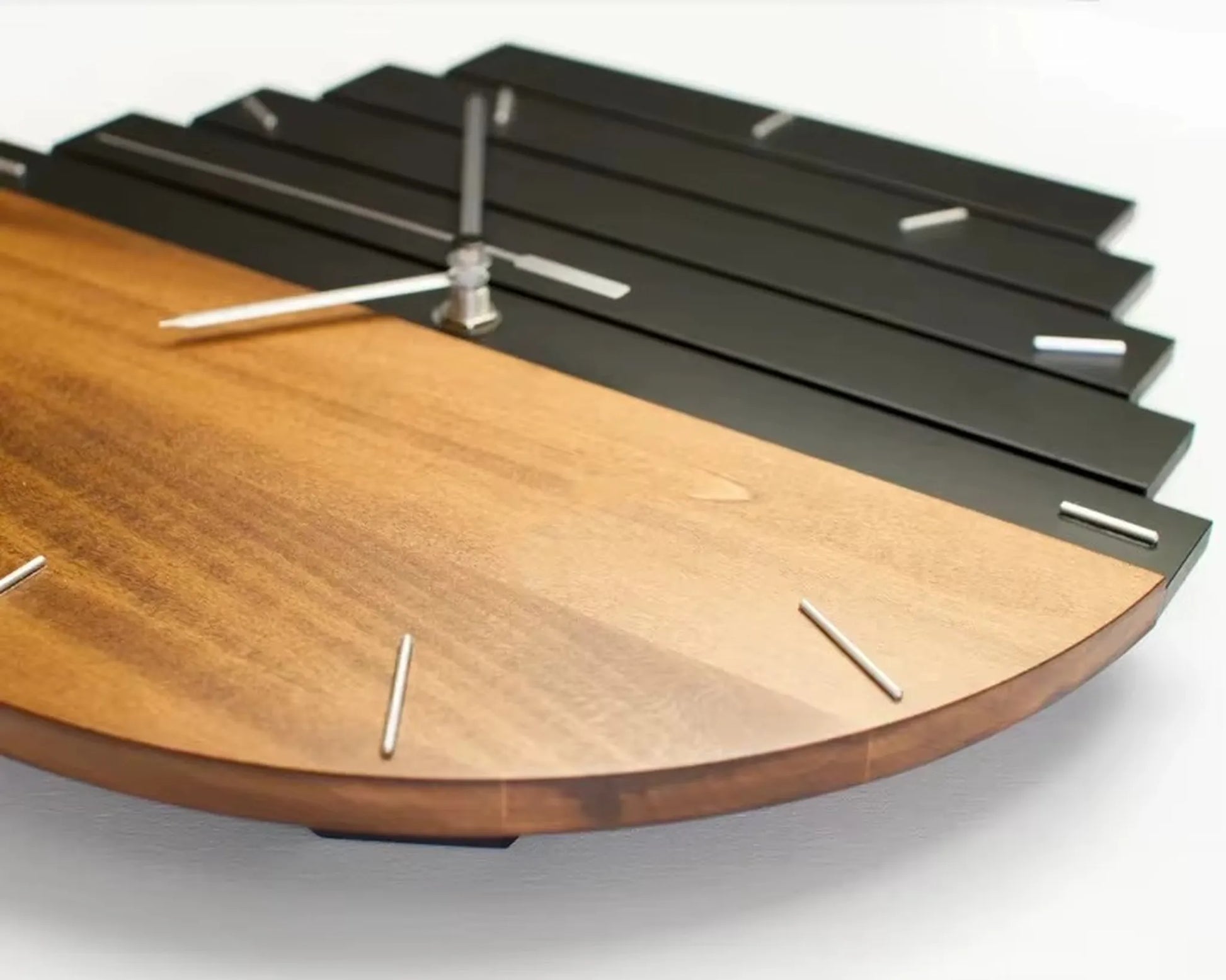 Modern wood wall clock - Clevor, featuring a round face with contrasting wood and black metal halves, marked by metal hour pins, and silver hour and minute hands, exemplifying sophisticated craftsmanship.