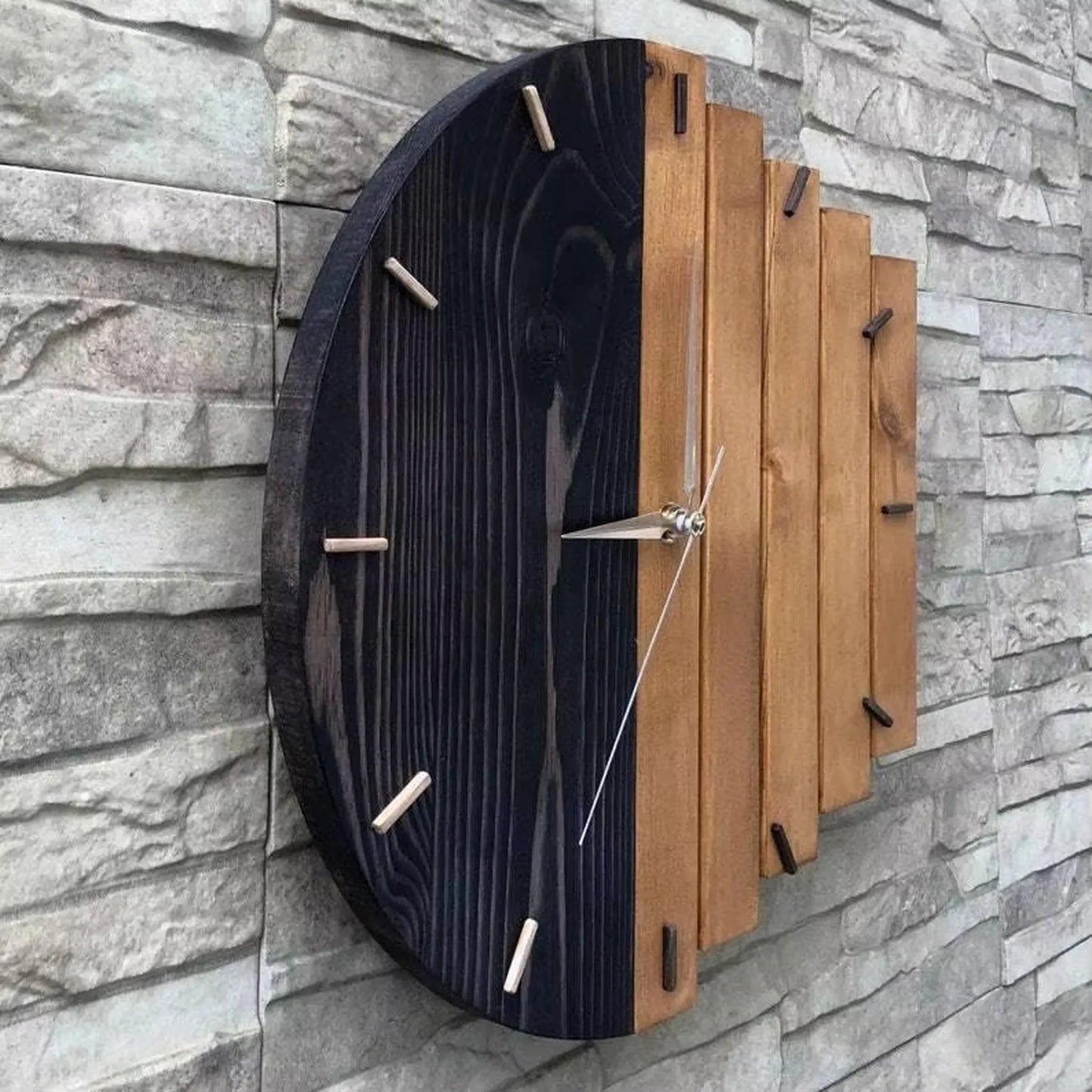 Modern wood wall clock - Clevor, featuring a circular design with a dual-tone face of black-stained and natural wood slats, complemented by cylindrical wooden hour markers and sleek metal hands.