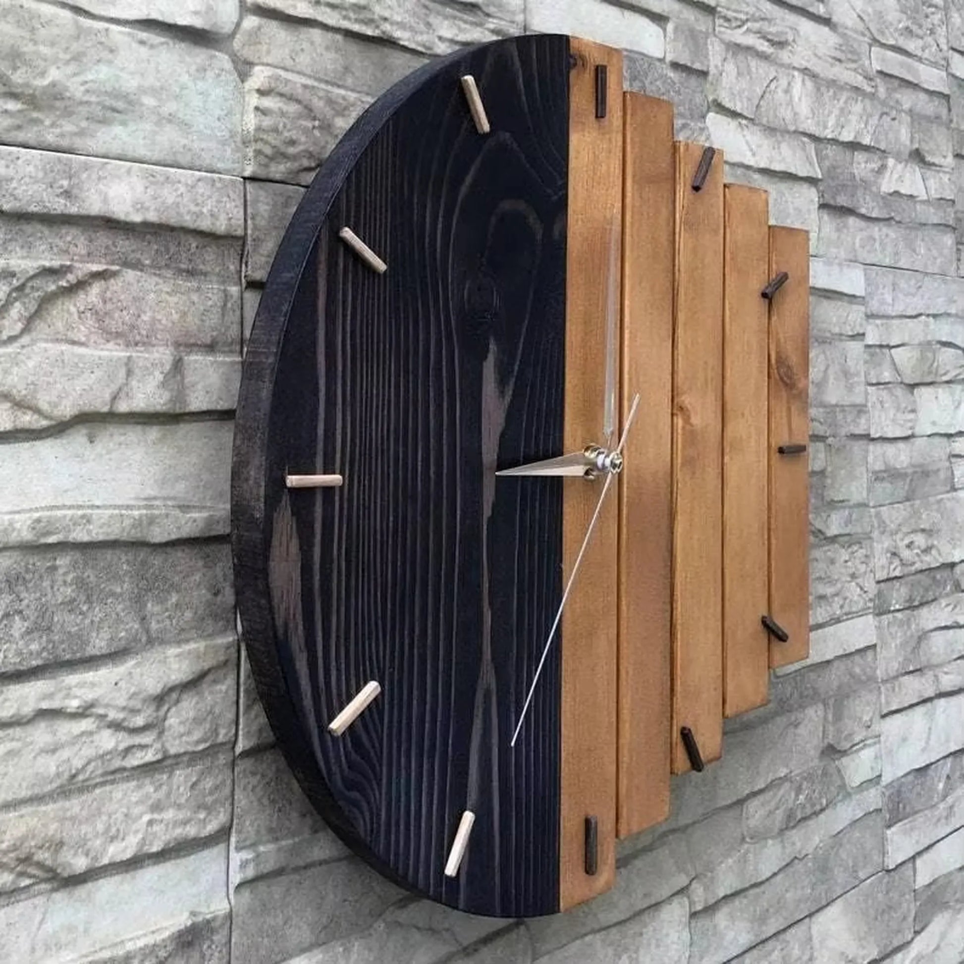 Modern wood wall clock - Clevor, featuring a circular design with a dual-tone face of black-stained and natural wood slats, complemented by cylindrical wooden hour markers and sleek metal hands.