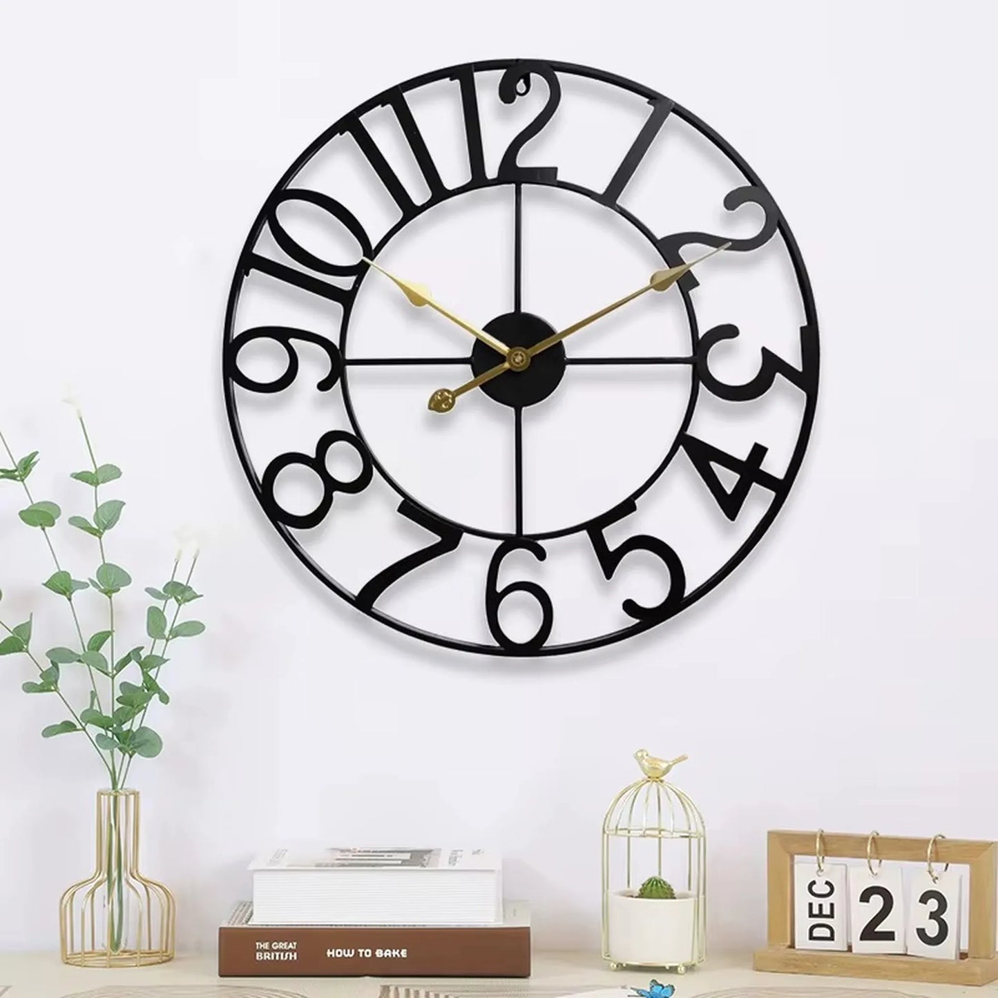 Oversized Wall Clock - Alderton: A round, open-framework metal clock with playful black numerals and slender gold hands, centered above a modern vignette with books, a vase, and a perpetual calendar.