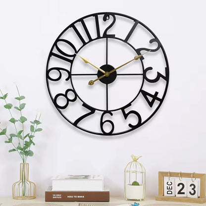 Oversized Wall Clock - Alderton: A round, open-framework metal clock with playful black numerals and slender gold hands, centered above a modern vignette with books, a vase, and a perpetual calendar.