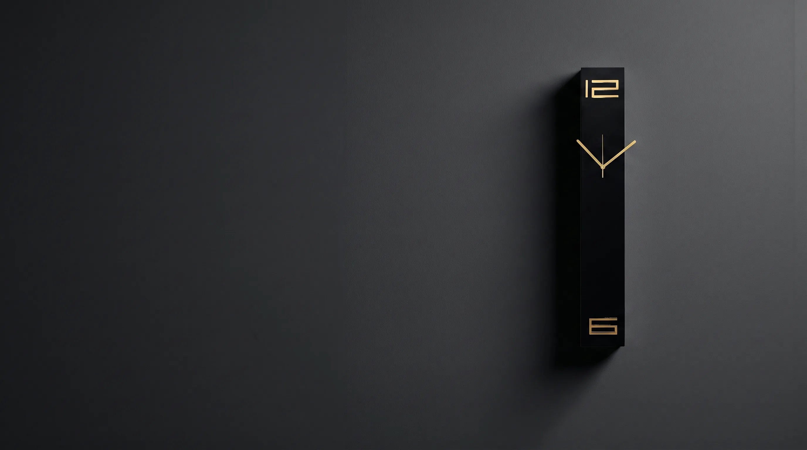 Black rectangular wall clock with brass numerals on a dark plaster wall in raking light
